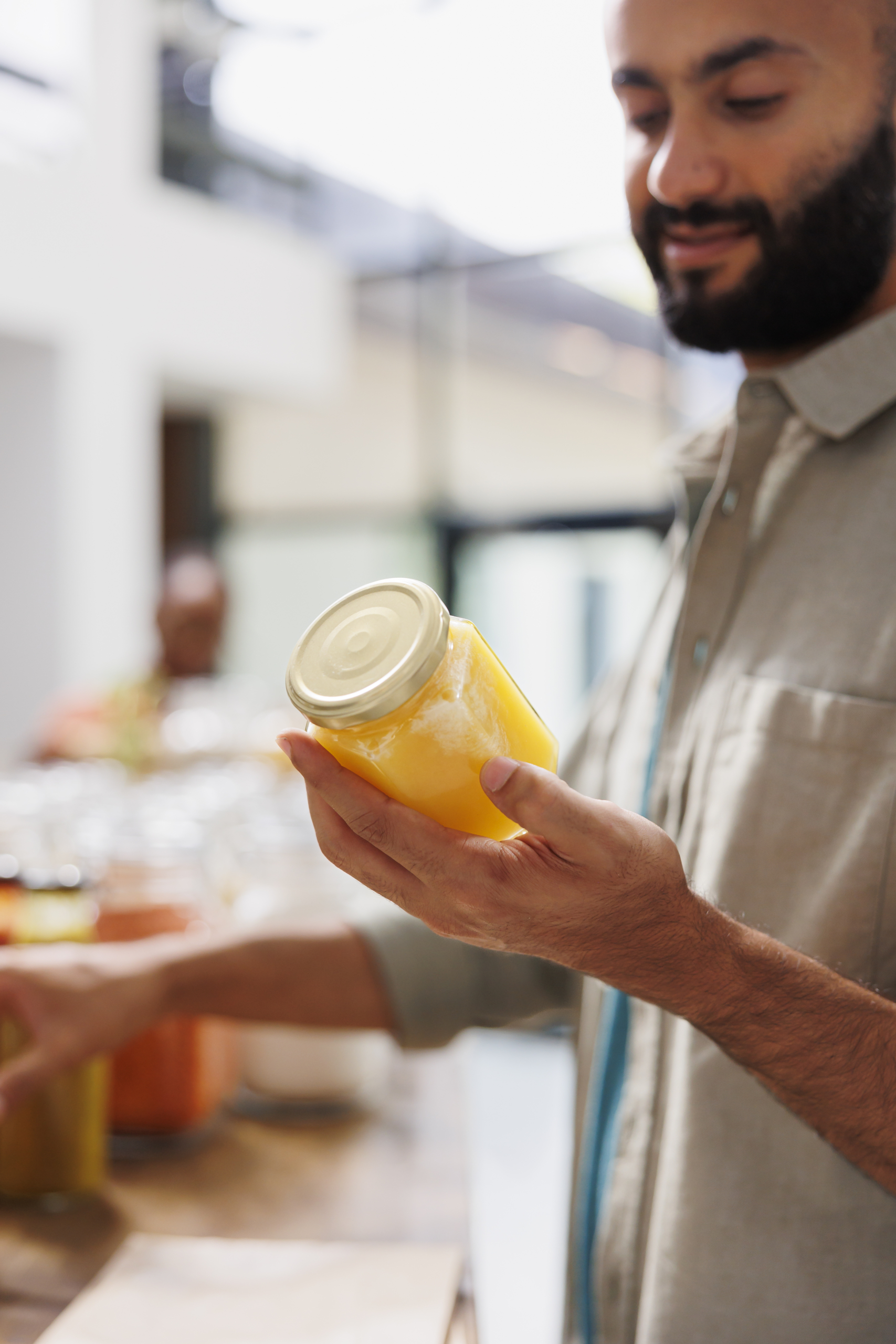 Male customer holding and looking closely at a glass jar filled with an organic product in grocery store. Close-up of young man grasping plastic free container with natural honey.